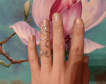 May include: A silver ring with a swirling design. The ring is worn on the index finger of a hand.