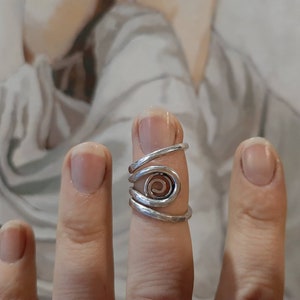May include: A silver ring with a spiral design. The ring is worn on the index finger of a hand.