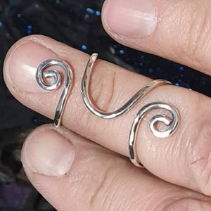Op de afbeelding: Een zilveren ring met een uniek ontwerp met twee spiralen. De ring wordt aan een vinger gedragen.