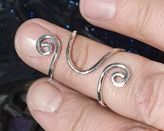 May include: A silver ring with a unique design featuring two spirals. The ring is worn on a finger.