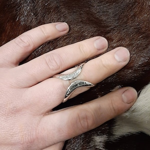 May include: A silver ring with a hammered finish and a unique open design. The ring is worn on the index finger.