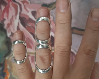 Op de afbeelding: Drie zilveren ringen die aan een vinger worden gedragen. De ringen zijn open en hebben een rechthoekige vorm.