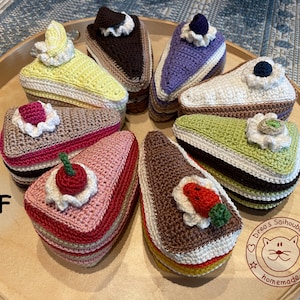 Op de afbeelding: Een verzameling van acht gehaakte taartpunten op een houten dienblad. De taarten zijn versierd met verschillende toppings, waaronder kersen, aardbeien, blauwe bessen en slagroom. De taarten zijn allemaal in verschillende kleuren, waaronder roze, bruin, groen, geel en paars. Het dienblad heeft een bruine houten afwerking en een wit label met de tekst "Drea's Saiboubaiko homemade".