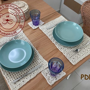 Könnte beinhalten: Zwei gehäkelte Tischsets mit einem gehäkelten Untersetzer auf einem Holztisch. Ein blaues Glas und ein blauer Teller befinden sich auf den Tischsets. Der Text "Drea's Saihoubaka homemade" befindet sich in einem roten Kreis auf dem Tisch. Der Text "PDF" befindet sich in braunem Text auf dem Tisch.
