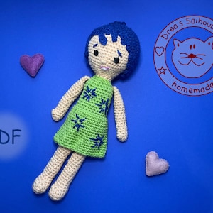 Könnte beinhalten: Häkelpuppe mit blauen Haaren und einem grünen Kleid mit blauen Sternen. Die Puppe liegt auf einem blauen Hintergrund mit zwei lila Herzen und einem weißen Kreis mit dem Text "PDF" darin. Der Kreis enthält auch den Text "Drea's Saihoubako homemade" in rot.