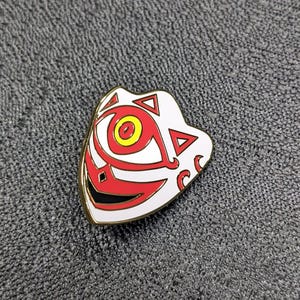 May include: A white and red enamel pin with a stylized eye design. The eye is red with a yellow center and is surrounded by a white mask with black details.