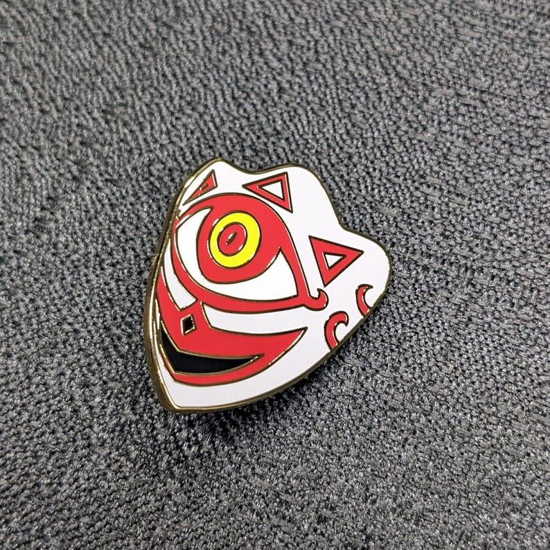 May include: A white and red enamel pin with a stylized eye design. The eye is red with a yellow center and is surrounded by a white mask with black details.