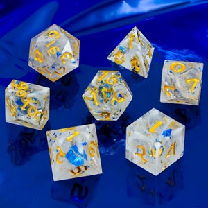 May include: Set of seven white dice with gold and blue glitter accents. The dice are numbered 1 through 6.