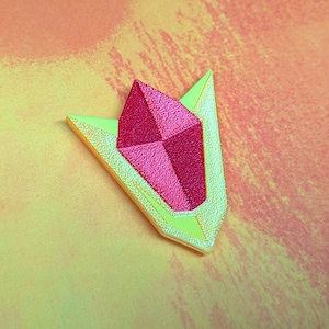 May include: A geometric-shaped brooch with a textured, metallic pink gemstone center and a light green and gold border. The brooch is set against a yellow and orange background.