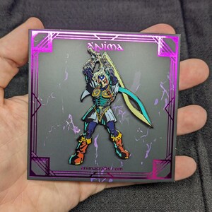Op de afbeelding: Een zwarte en zilveren emaille pin met een personage uit het videospel "The Legend of Zelda: Majora's Mask". Het personage houdt een zwaard vast en heeft een blauw en groen kleurenschema. De pin is geplaatst op een zwarte achtergrond met een paarse rand en de tekst "animacrafts.com".