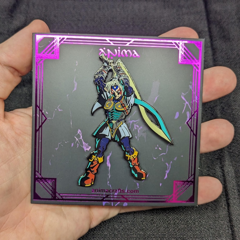 Op de afbeelding: Een zwarte en zilveren emaille pin met een personage uit het videospel "The Legend of Zelda: Majora's Mask". Het personage houdt een zwaard vast en heeft een blauw en groen kleurenschema. De pin is geplaatst op een zwarte achtergrond met een paarse rand en de tekst "animacrafts.com".