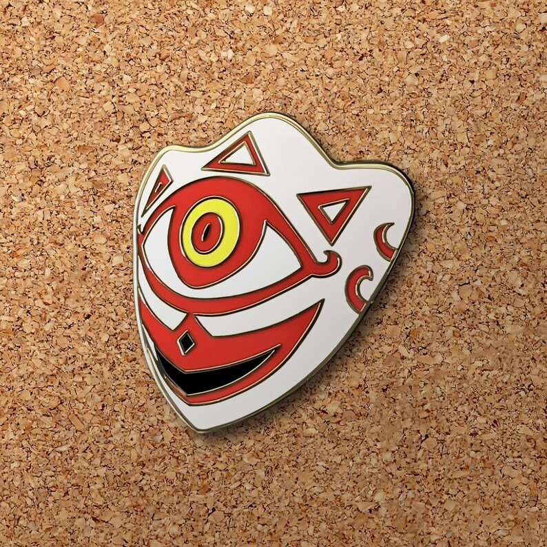 May include: A white enamel pin with a red and yellow design. The pin features a stylized eye with a red iris and a yellow pupil. The eye is surrounded by a white background with red and gold accents. The pin is shaped like a mask.