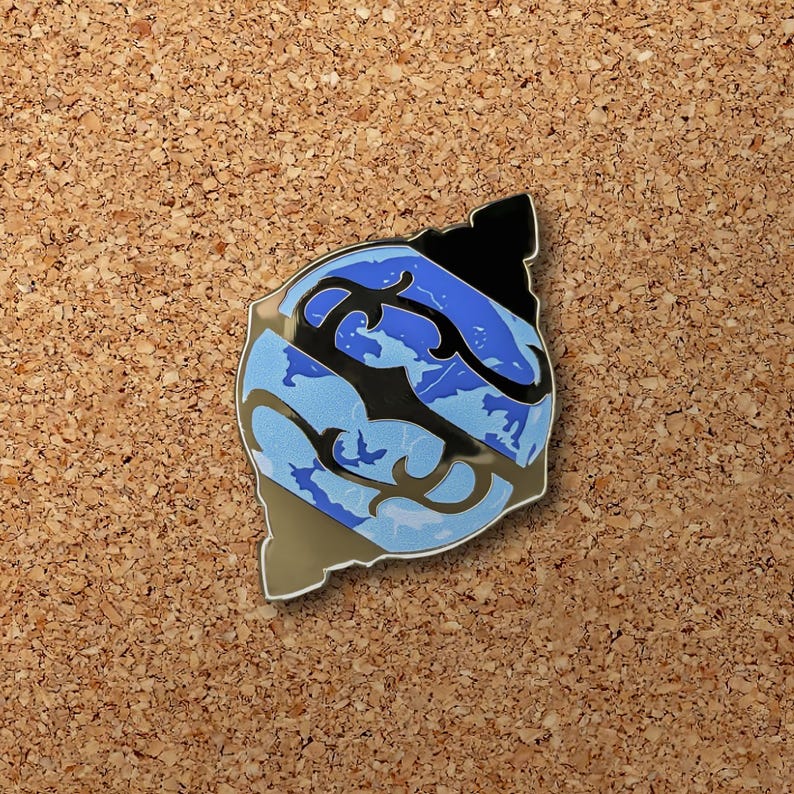 May include: A blue and black enamel pin with a stylized design of a wave or ocean. The pin has a shiny, metallic finish.