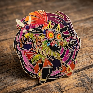 May include: A circular metal enamel pin featuring a colorful character with a mask, large yellow eyes, and spiky hair, surrounded by a swirling purple and pink background with a small winged insect figure on the upper left side of the design.