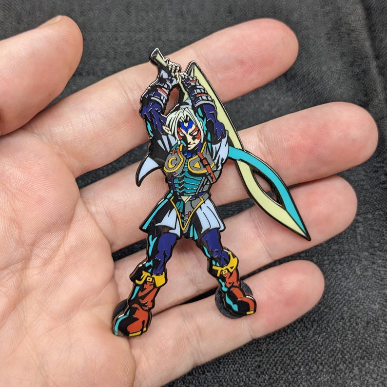 Op de afbeelding: Een blauwe en groene emaille pin met een personage uit de Legend of Zelda-videogameserie. Het personage houdt een zwaard vast en heeft een blauw en rood masker.