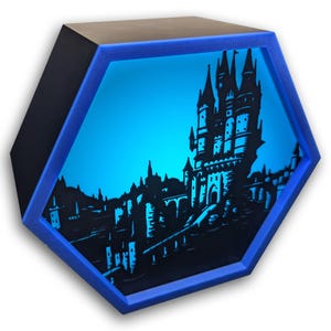 Puede incluir: Arte mural hexagonal negro y azul iluminado, con una silueta de castillo y paisaje urbano sobre un fondo azul brillante. El marco es azul vibrante y la obra de arte está iluminada.