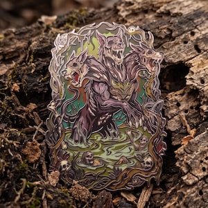 May include: A metal enamel pin featuring a three-headed creature with skeletal canine features emerging from a swampy green pool. The design includes intricate details of twisted branches, skulls, and murky water, rendered in shades of purple, green, and brown.