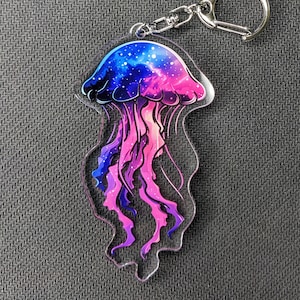 Peut inclure: Un porte-clés en acrylique transparent avec une méduse à thème galaxie violette et bleue avec un anneau de clé en métal argenté.