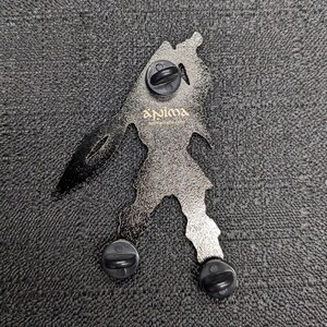 Op de afbeelding: Een zilverkleurige metalen pin met een gestileerd figuur dat een zwaard vasthoudt. De pin heeft een zwarte achterkant met drie zwarte pin-ruggen. De pin heeft de tekst "Anima" in gouden letters.