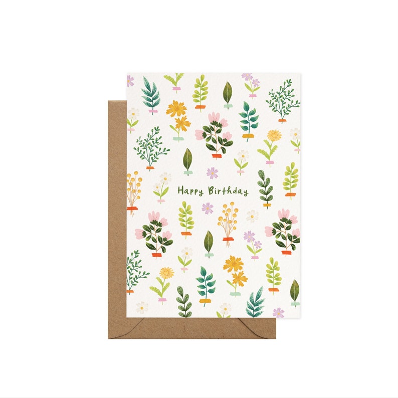 K&ouml;nnte beinhalten: Eine Geburtstagskarte mit floralem Muster und dem Schriftzug "Happy Birthday". Die Karte zeigt verschiedene Blumen und Bl&auml;tter in Rosa, Gelb, Gr&uuml;n und Lila auf wei&szlig;em Hintergrund. Sie wird von einem braunen Umschlag begleitet.