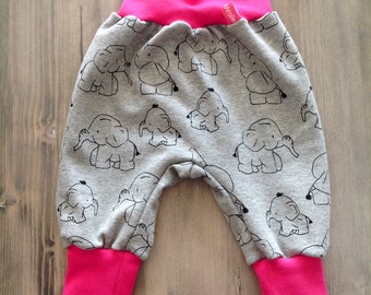 Op de afbeelding: Grijze babybroek met een roze tailleband en boorden. De broek heeft een patroon van zwarte olifanten. De tailleband heeft een klein wit label met het woord "wolle" erop.