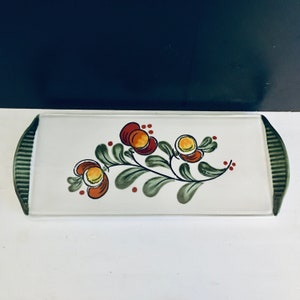 Könnte beinhalten: Ein weißes Keramik-Serviertablett mit grünem Rand und handbemaltem Blumendesign mit roten, orangefarbenen und gelben Blüten mit grünen Blättern und roten Beeren.