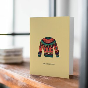 Può includere: Un biglietto giallo con un'illustrazione di un maglione colorato e fantasia e il testo "Shame it's 40 degrees outside".