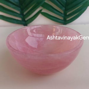 Puede incluir: Un cuenco de cuarzo rosa. El cuenco es liso y pulido, con un ligero brillo. El cuenco tiene un diámetro de unos 10 cm.