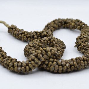 Puede incluir: Un collar largo hecho de pequeñas cuentas marrones con forma de semillas enhebradas en un cordón beige delgado.