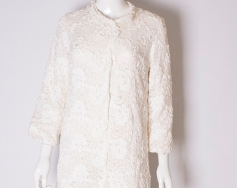 May include: A white lace coat with a button closure. The coat is on a white mannequin.