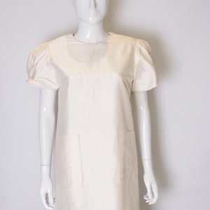 May include: A white sleeveless dress with a round neckline and two pockets. The dress has a slightly puffed sleeve detail.