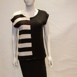 Könnte beinhalten: Ein schwarz-weiß gestreiftes Shirt mit einem schwarzen Rock. Das Shirt hat einen runden Ausschnitt und kurze Ärmel.