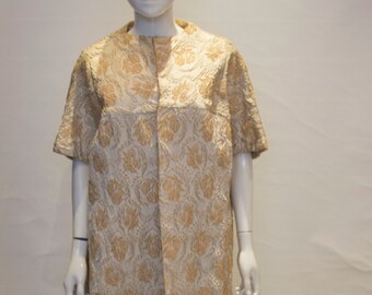 May include: A white dress with a gold floral pattern. The dress has a short sleeve and a button-up front.