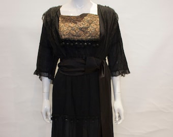 May include: A black dress with a lace bodice and a black satin sash. The dress has a tiered skirt and is decorated with black beads.