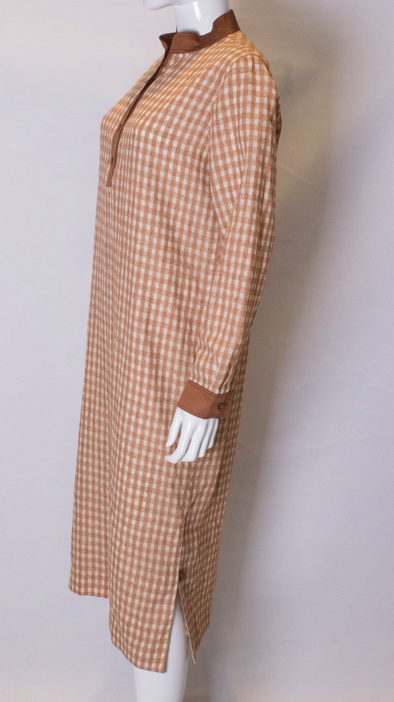 May include: A brown and white gingham long-sleeved dress with a brown collar and cuffs.