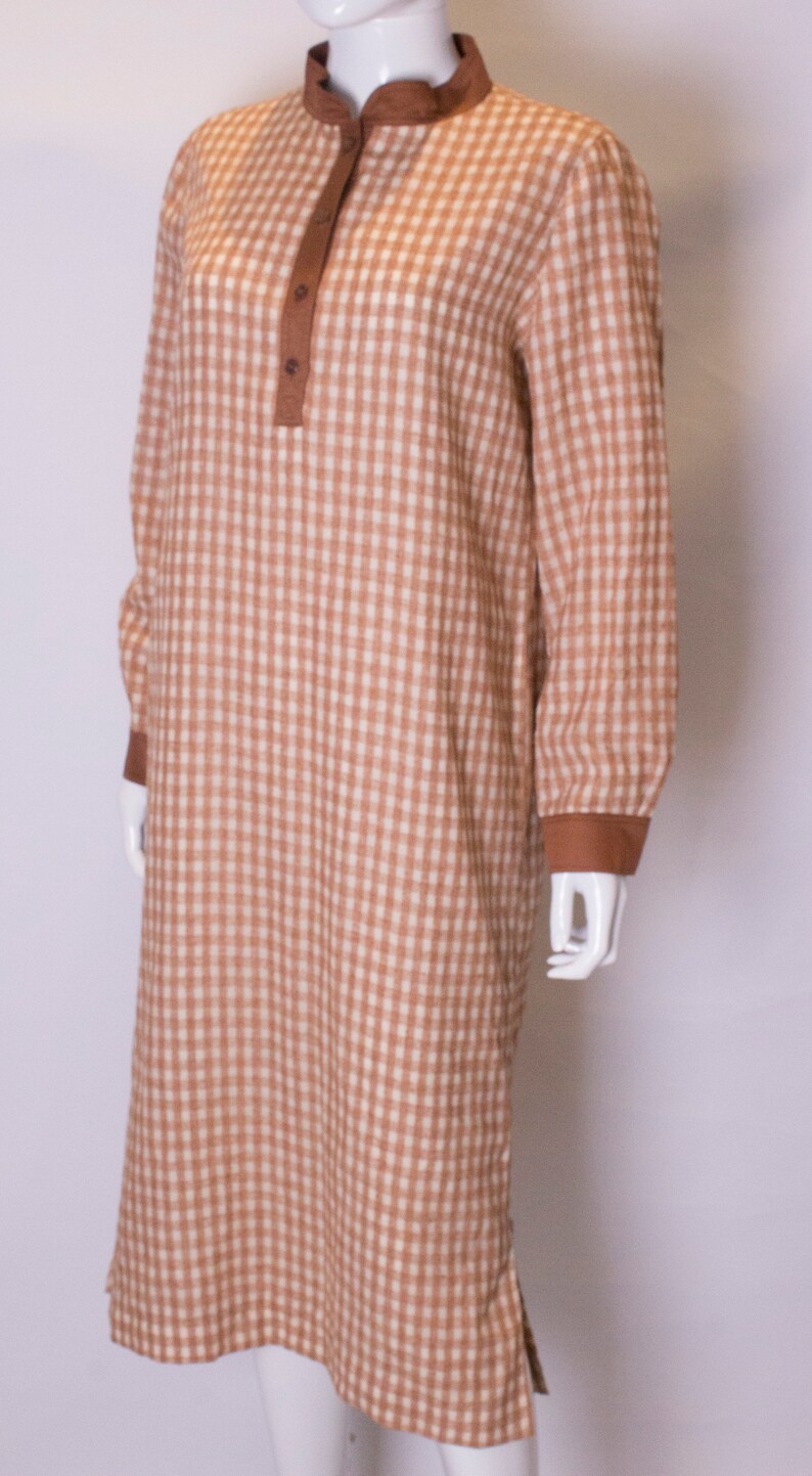 May include: A brown and white gingham long-sleeved dress with a brown collar and button closure.