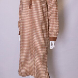 May include: A brown and white gingham dress with a brown collar and button closure. The dress has long sleeves and a loose fit.