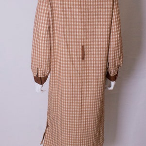 May include: A brown and white gingham dress with a brown collar and cuffs. The dress is on a white mannequin.