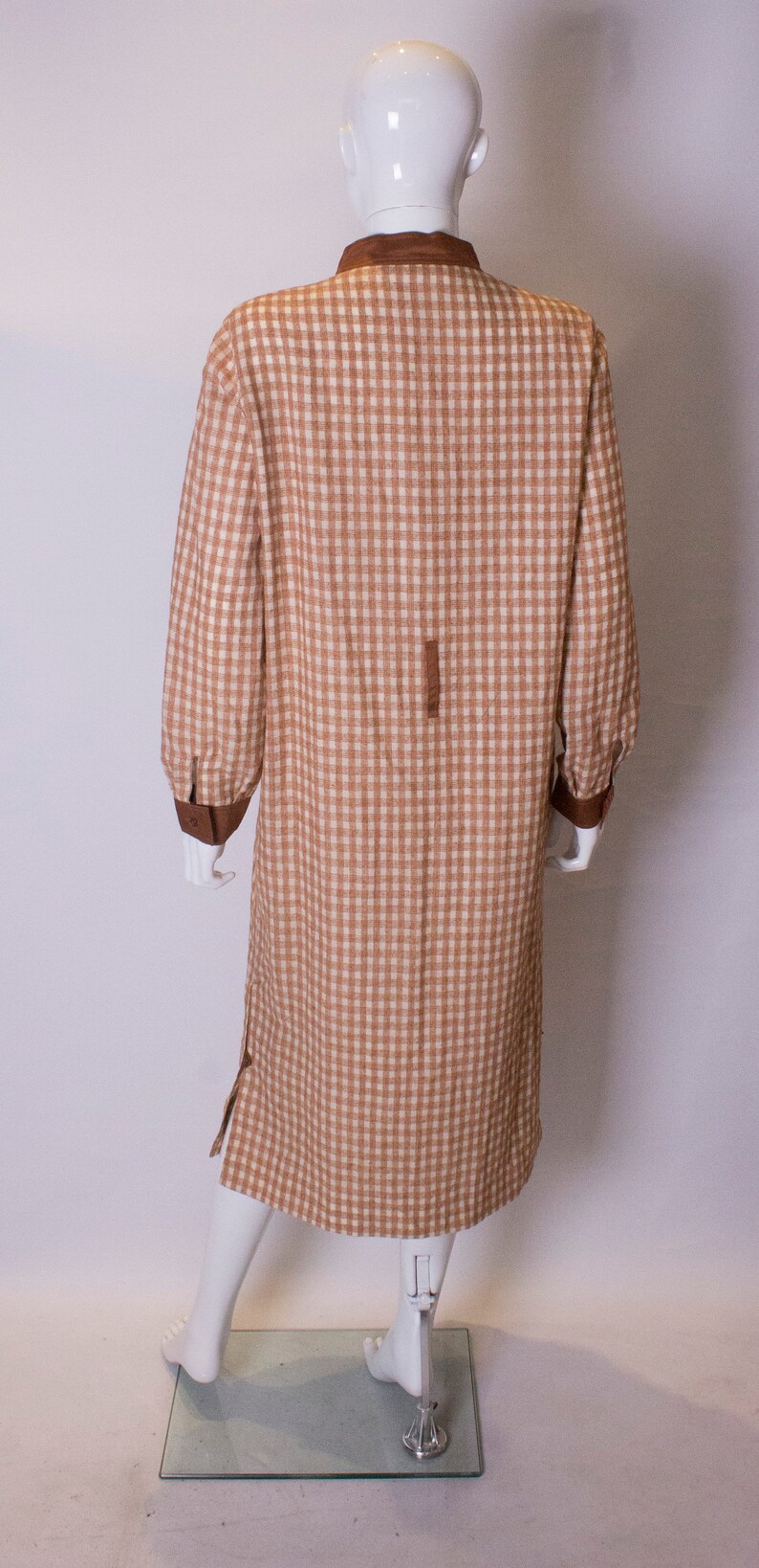 May include: A brown and white gingham dress with a brown collar and cuffs. The dress is on a white mannequin.