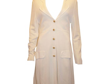 May include: A long white knitted cardigan with a V-neck, long sleeves, and a button-up front. The cardigan has two pockets on the front and a slightly flared hem.