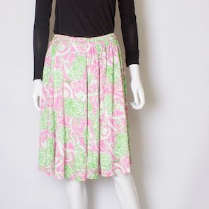 Puede incluir: Una falda estampada en rosa y verde con una camisa negra de manga larga en un maniquí blanco.