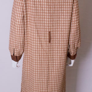 May include: A long brown and white gingham dress with a brown collar and cuffs. The dress has a button closure at the front and a slit on each side.