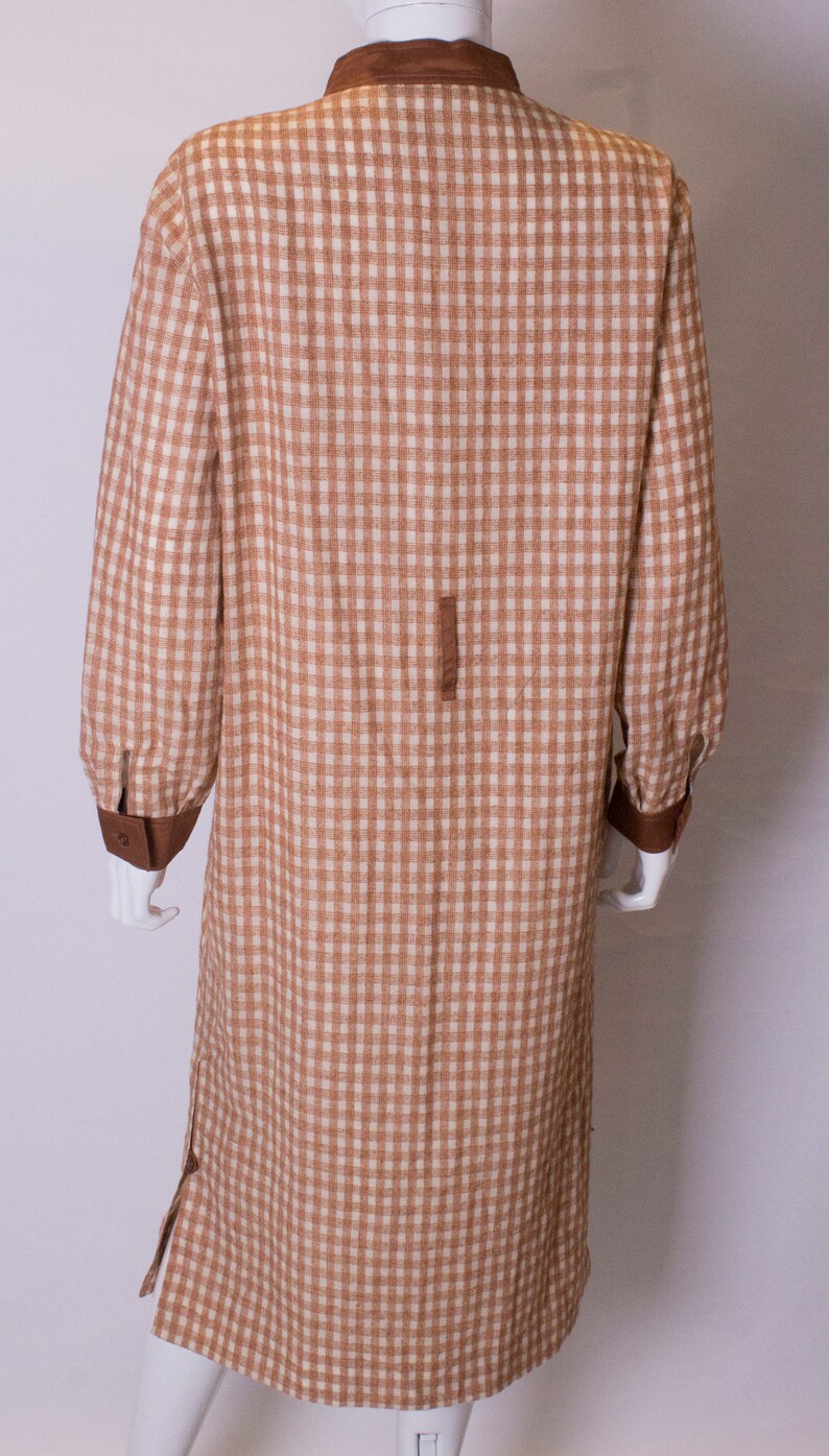 May include: A long brown and white gingham dress with a brown collar and cuffs. The dress has a button closure at the front and a slit on each side.