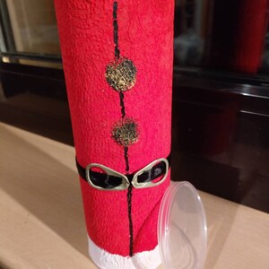 Może przedstawiać: Czerwono-biały kartonowy tubus z czarnym paskiem i złotymi k&oacute;łkami. Tubus ma biały rant i przezroczystą plastikową pokrywkę.