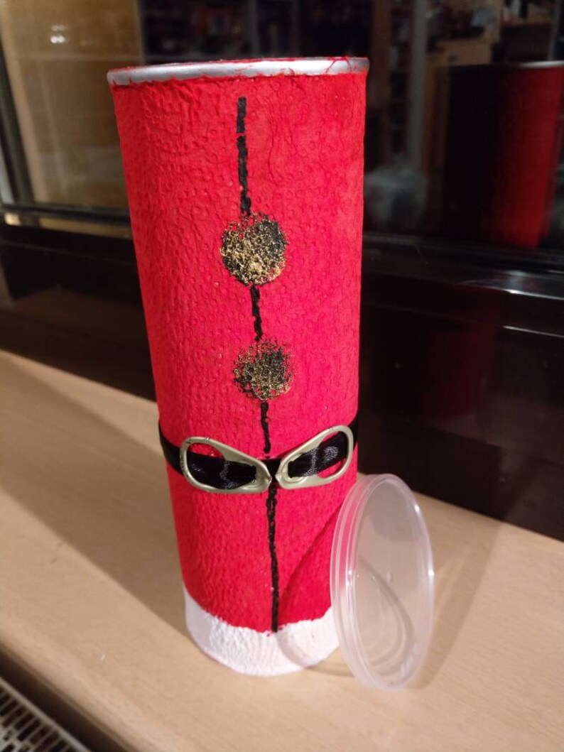 Może przedstawiać: Czerwono-biały kartonowy tubus z czarnym paskiem i złotymi k&oacute;łkami. Tubus ma biały rant i przezroczystą plastikową pokrywkę.