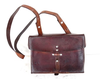 May include: A brown leather satchel with a long adjustable strap. The bag has a flap closure with a buckle and metal accents.