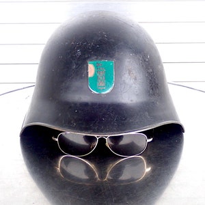 May include: A black military helmet with a green and white emblem on the front. The helmet is sitting on a table with a pair of sunglasses resting on top.