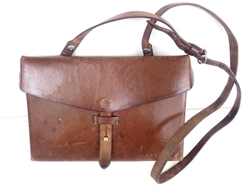 May include: A brown leather satchel with a long strap. The bag has a flap closure and a metal buckle.