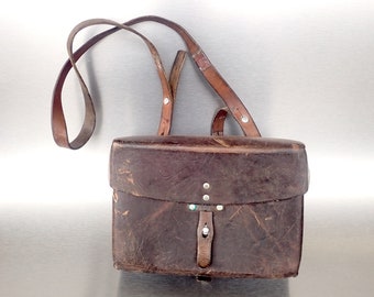 May include: A brown leather satchel with a long strap. The bag has a flap with a buckle and is worn and distressed.