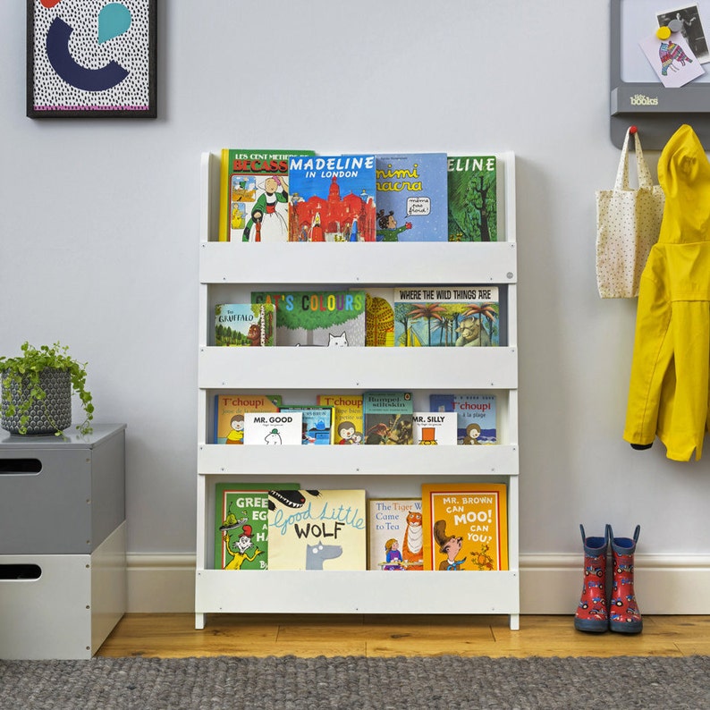 May include: White bookshelf with four shelves, filled with children's books. The books have colorful covers with titles like "Madeline in London", "Where the Wild Things Are", and "Good Little Wolf".